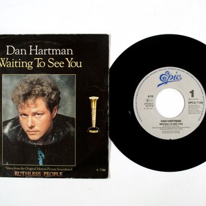 Peut inclure: Un disque vinyle et sa pochette avec "Waiting To See You" de Dan Hartman. La pochette est noire avec le titre de la chanson et le nom de l'artiste en blanc. L'étiquette du disque est blanche avec du texte noir et le logo Epic.