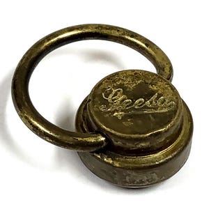 May include: Aged brass-toned metal pull with a circular handle and a round base. The base features the word "Apeda" in an elegant script. The metal shows signs of wear, giving it a vintage appearance.