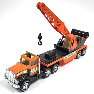 Peut inclure: Camion grue jouet orange et noir avec le texte "B&L Construction" et "Big Brute Crane". Le camion a un bras de grue, un crochet et plusieurs roues. La cabine est orange avec une calandre argentée.