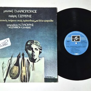 Puede incluir: Álbum de vinilo vintage con una etiqueta azul y blanca. La portada del álbum presenta un busto clásico, instrumentos musicales y texto griego. El disco es negro y tiene una etiqueta azul con texto blanco.