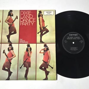 May include: A vintage vinyl record album titled "Dixie Land Dance Party" by The Sandy Stompers. The album cover shows a woman in a fringed skirt and orange top, holding a clarinet. A black vinyl record is next to the album.