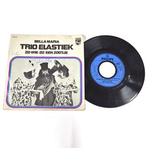 Può includere: Un disco in vinile a 45 giri di Trio Elastiek intitolato Bella Maria e Zo-Wie-Zo Een Zootje. La copertina quadrata in carta presenta una fotografia in bianco e nero di tre artisti in costume da clown, con un'etichetta blu Philips sul disco.