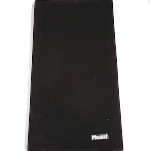 May include: A rectangular black speaker cover with a textured surface. The cover features a silver "Magnat" logo in the lower right corner. The speaker cover is designed to protect the speaker.