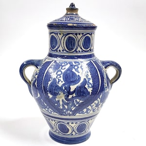 Pode incluir: Um vaso de cerâmica azul e branco com tampa. O vaso apresenta um design floral detalhado em azul sobre um fundo branco. Possui duas alças e uma borda decorativa. A tampa também é decorada com padrões azuis e brancos.