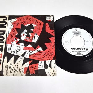Può includere: Un disco in vinile vintage e la sua copertina. La copertina mostra il nome della band "COLDCUT" in bianco, con il titolo della canzone "Stop This Crazy Thing" in rosso. Il disco è nero con un'etichetta bianca.
