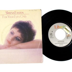 May include: A vintage vinyl record and sleeve featuring Sheena Easton's "For Your Eyes Only." The album cover displays a portrait of a woman. The black vinyl record is next to the album cover.
