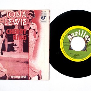 May include: A vinyl record and album cover. The album cover features a photo of a man in sunglasses and the text "Jona Lewie Cherry Ring After We Swun". The record is black with a green and yellow label.