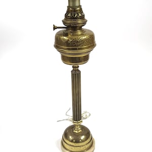 May include: An antique brass oil lamp with a detailed floral design on the reservoir. The lamp features a tall, fluted column and a round base. The top has a threaded opening for a wick. The lamp is a vintage piece.