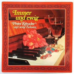 May include: A vintage album cover with a red border features the text "Immer und ewig" and "Peter Kreuder und seine Solisten." The image includes two wine glasses filled with red liquid, a red flower, and piano keys. Decorative gems are scattered on the piano.