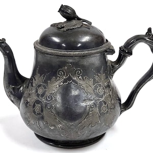 Puede incluir: Una tetera de plata con un diseño floral ornamentado y una tapa con un pomo en forma de capullo.