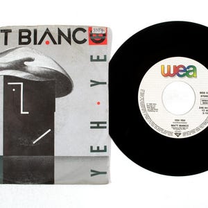Peut inclure: Un disque vinyle vintage et sa pochette. La pochette affiche le nom du groupe "Matt Bianco" en noir avec des accents rouges. L'illustration est une représentation stylisée d'une personne portant un chapeau. Le disque est noir avec une étiquette blanche.