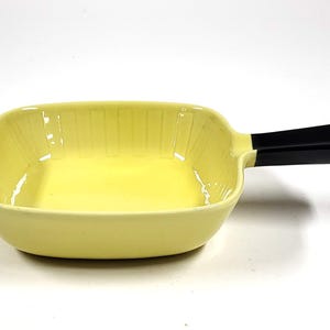Peut inclure: Un plat à four en céramique jaune avec une poignée noire. Le plat est de forme carrée et a un intérieur côtelé.