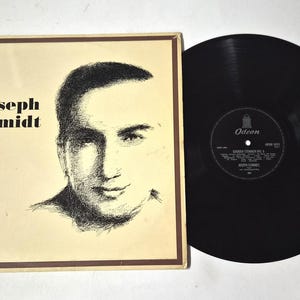 May include: A vintage vinyl record and album cover. The album cover is beige with the text "Golden Stemmen 6" and "Joseph Schmidt". A black vinyl record is next to the album cover. The record label is visible.