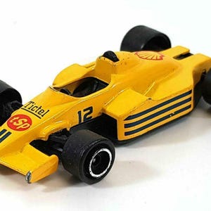 May include: A yellow toy race car with black wheels and accents. The car features the number 12, the Shell logo, and the text "Tictel Sp". The car has black stripes on the side.