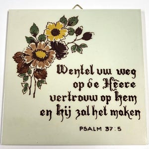 Può includere: Piastrella quadrata in ceramica con un motivo floreale nei toni del marrone, giallo e verde. La piastrella presenta testo in scrittura marrone scuro, tra cui "PSALM 37:5". Un gancio di metallo è attaccato per appenderla.