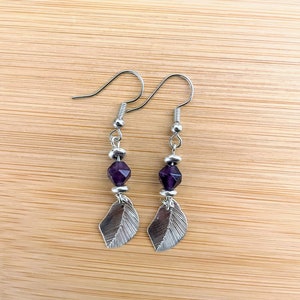 May include: A pair of silver earrings with a purple gemstone and a leaf charm.