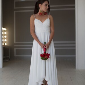 May include: A bride wearing a white wedding dress with a high-low hemline and red shoes. She is holding a bouquet of red flowers.