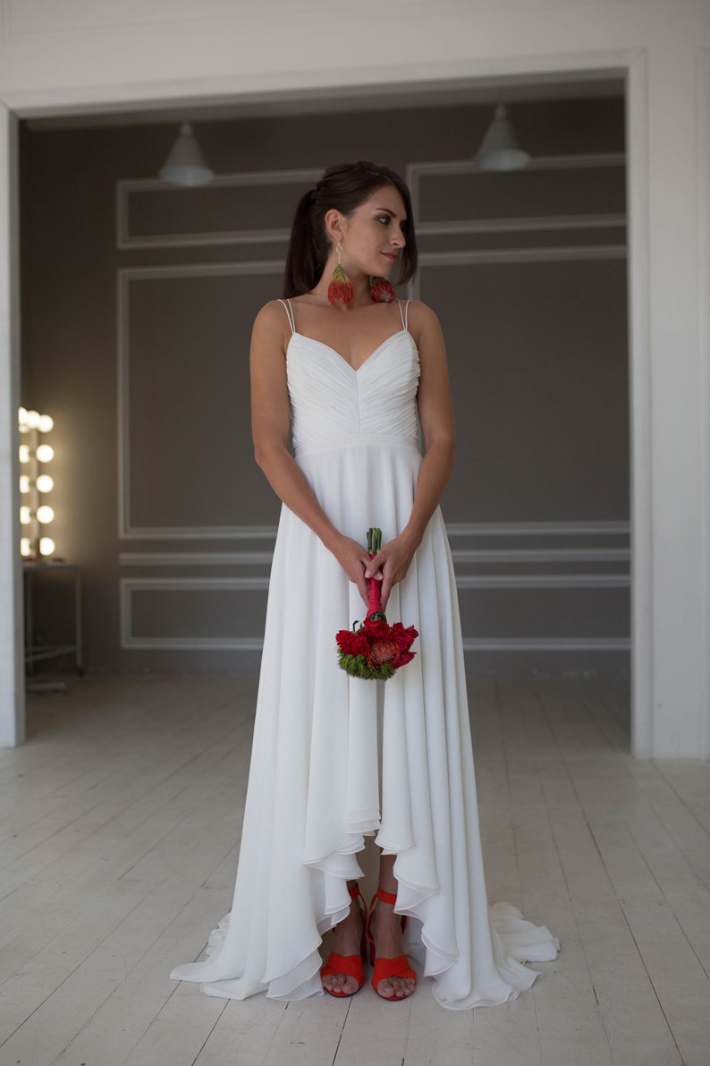 May include: A bride wearing a white wedding dress with a high-low hemline and red shoes. She is holding a bouquet of red flowers.