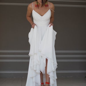 May include: A white wedding dress with a ruffled skirt and a sweetheart neckline. The dress is being held up by the person wearing it, revealing red high-heeled sandals.