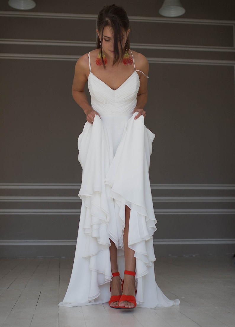 May include: A white wedding dress with a ruffled skirt and a sweetheart neckline. The dress is being held up by the person wearing it, revealing red high-heeled sandals.