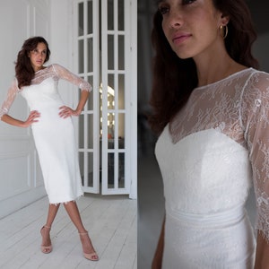 Può includere: Un abito da sposa bianco in pizzo con un corpetto aderente e una gonna che arriva al ginocchio. L'abito ha un'applicazione in pizzo e una scollatura rotonda.