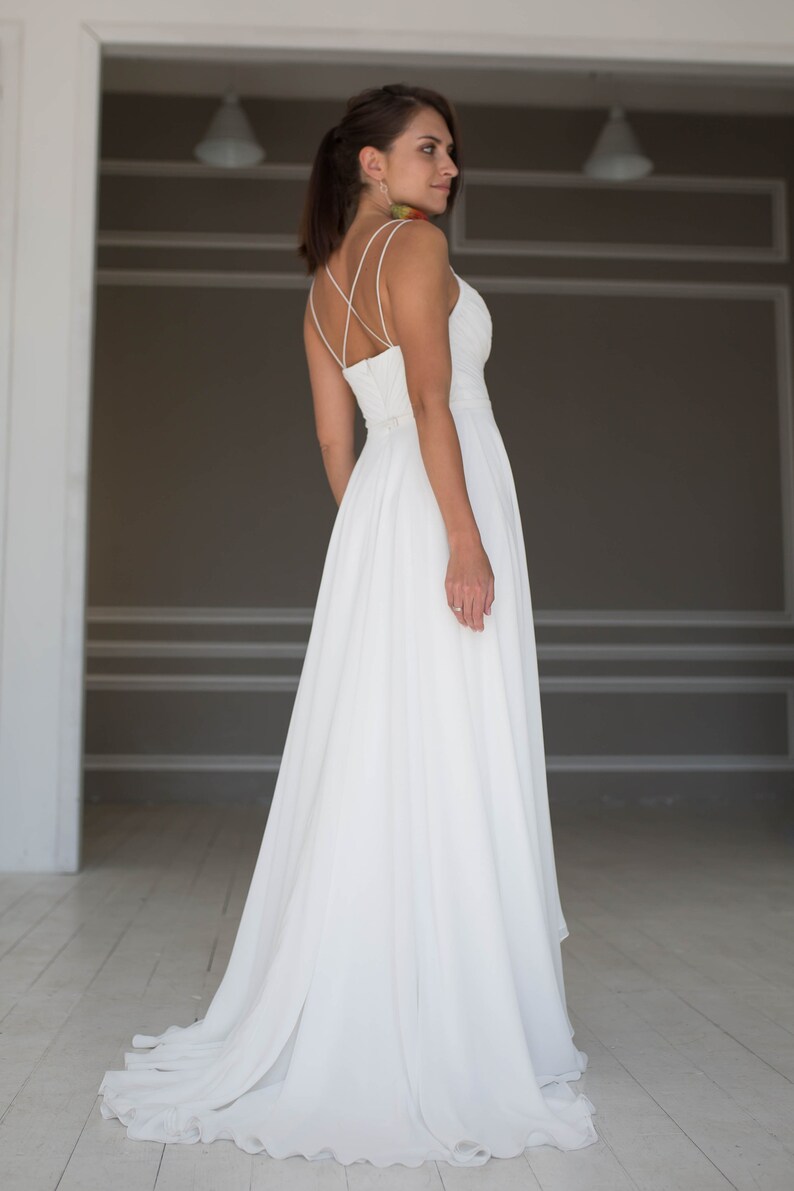 May include: A white wedding dress with a simple, elegant design. The dress has a fitted bodice with a low back and a flowing skirt.