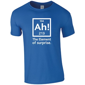 May include: A royal blue t-shirt featuring a white graphic of a periodic table element. The element is labelled "Ah!" with the atomic number 104 and atomic weight 213. The text below the element reads "The Element of surprise."