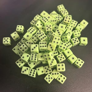 May include: A large collection of small, square, light green dice with rounded corners and black pips. Each die features standard six-sided numbering with black dots arranged in various patterns across the faces, scattered in a loose pile.