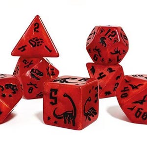 Puede incluir: Un juego de siete dados poliédricos rojos con acabado brillante y marcas en tinta negra. Cada dado presenta siluetas de dinosaurios, huellas y números en negro. El conjunto incluye un d4, d6, d8, d10, d12, d20 y un dado de porcentaje.