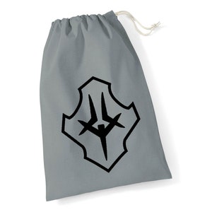 May include: A grey drawstring bag featuring a black graphic design. The design is a stylised shield shape with a central figure and cross-like elements. The bag has a white drawstring closure.