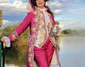Op de afbeelding: Een levendige fuchsia jas met ingewikkeld bloemenborduursel en gouden randen, gedragen over een bijpassende fuchsia broek. Het ensemble bevat een witte jabot met ruches, een driekante hoed met roze veren, een zwarte wandelstok met gouden handvat en een metalen pul.