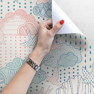 Puede incluir: Un rollo de papel tapiz con un dise&ntilde;o caprichoso que presenta nubes rosas y azules, p&aacute;jaros y patrones geom&eacute;tricos sobre un fondo crema.