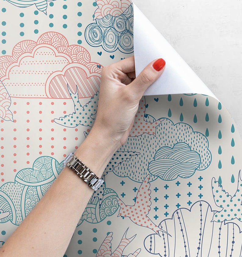 Puede incluir: Un rollo de papel tapiz con un dise&ntilde;o caprichoso que presenta nubes rosas y azules, p&aacute;jaros y patrones geom&eacute;tricos sobre un fondo crema.