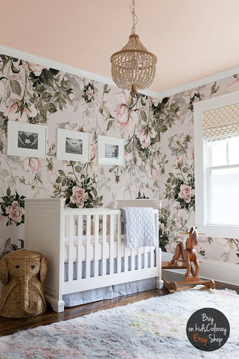 May include: A white crib with a floral wallpaper backdrop. The crib has a white mattress and a blue blanket. There is a wicker elephant toy basket next to the crib and a wooden rocking horse in the foreground. The text "Buy on kidsColoray Etsy Shop" is visible in the lower right corner of the image.