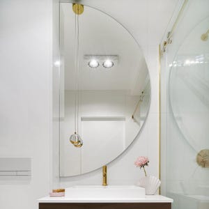May include: A white bathroom with a half-round mirror, gold fixtures, and a white porcelain sink. A pink flower is in a white vase on the counter.
