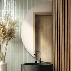 May include: A bathroom with green subway tiles, a round mirror, a black sink, and a wooden wall.