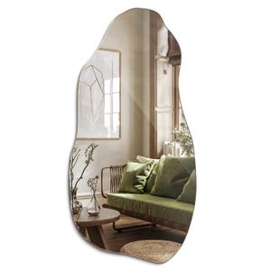 May include: A large, irregular-shaped mirror with a wavy, organic design. The mirror reflects a room with a green sofa, a wooden coffee table, and a vase of flowers.