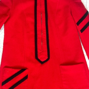 May include: A vibrant red dress with a high collar and long sleeves. The dress features black trim along the zipper and pockets, with black stripes on the sleeves and pockets. The dress has a zipper closure and two front pockets.