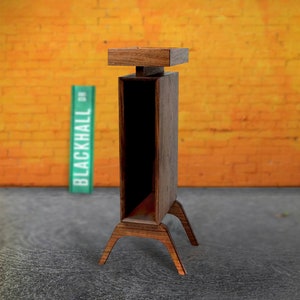 May include: A wooden stand with a square top and four legs. The stand is made of dark wood and has a natural finish. The stand is in front of a brick wall with a green and orange color scheme. The stand is labeled "BLACKHALL" in green.