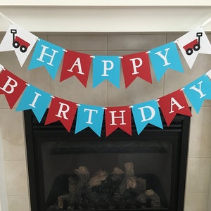 May include: A red and blue banner with white letters that reads "Happy Birthday". The banner is decorated with small red wagons with white wheels.