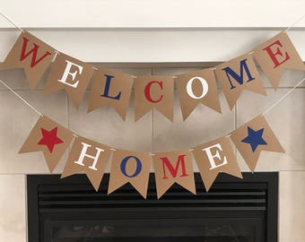 May include: A brown paper banner with the words "WELCOME HOME" in red, white, and blue letters. The banner is strung up above a fireplace.