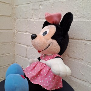 May include: A plush Minnie Mouse doll, featuring black ears, a pink bow, and a pink dress with white polka dots. The doll has white gloves, blue feet, and a smiling expression. A classic Disney character.