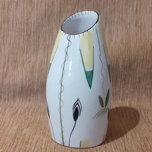 Peut inclure: Vase en céramique blanche avec une ouverture angulaire unique. Le vase est décoré d'un motif floral stylisé dans des tons de jaune, vert et marron.