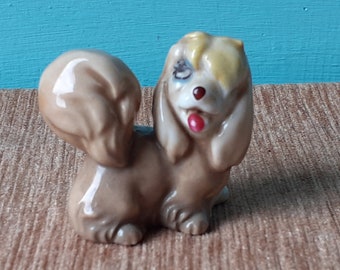 May include: A ceramic figurine of a brown and white dog with a yellow and white head. The dog has a red tongue sticking out and one blue eye.