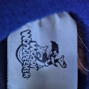 May include: White tag with a black and white cartoon image of Woody Woodpecker. The tag says "Woody Woodpecker" in a circular design.