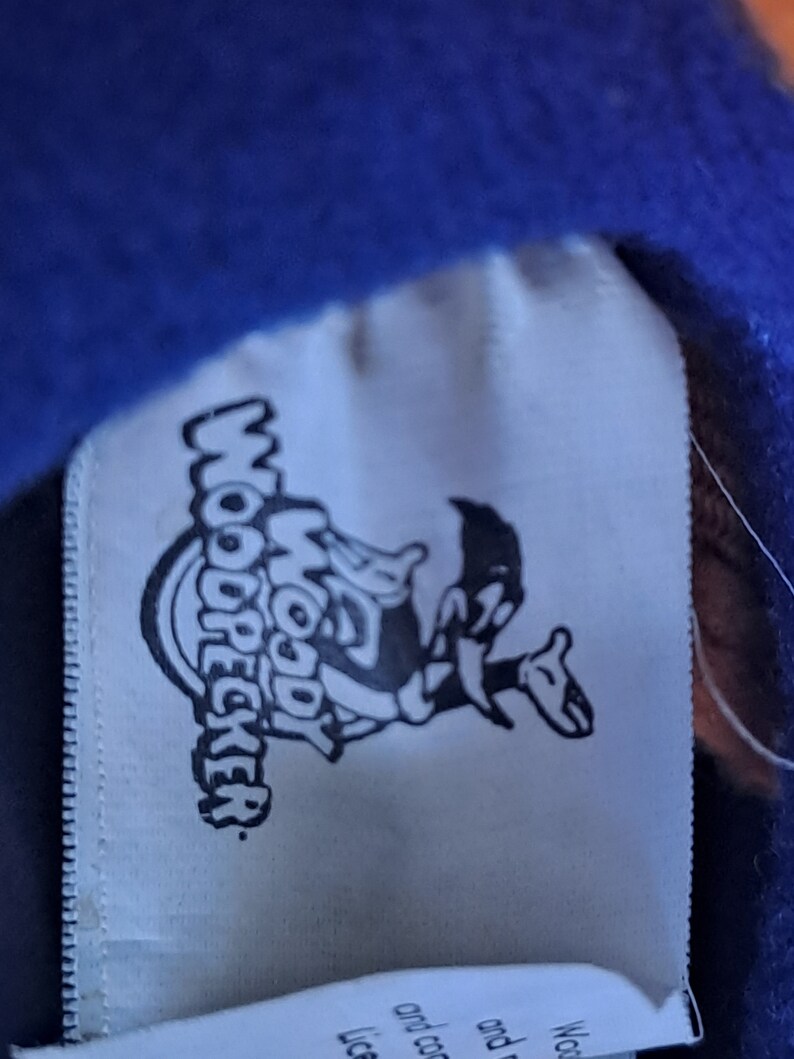 May include: White tag with a black and white cartoon image of Woody Woodpecker. The tag says "Woody Woodpecker" in a circular design.