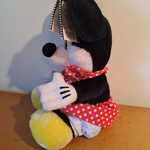May include: A plush toy of a cartoon mouse wearing a red and white polka dot dress and a black beret. The mouse is sitting with its legs crossed and has a yellow and black tail.