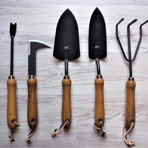 K&ouml;nnte beinhalten: F&uuml;nf Gartenger&auml;te mit Holzgriffen. Die Werkzeuge umfassen eine Schaufel, eine Handharke, einen Kultivator, eine kleine Handschaufel und einen Unkrautstecher.
