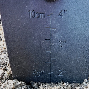 K&ouml;nnte beinhalten: Ein schwarzes Gartenwerkzeug mit einem Lineal, das in Zoll und Zentimetern markiert ist. Das Lineal zeigt Messungen von 2 Zoll bis 4 Zoll und von 5 Zentimetern bis 10 Zentimetern.