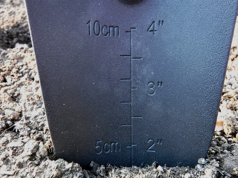 K&ouml;nnte beinhalten: Ein schwarzes Gartenwerkzeug mit einem Lineal, das in Zoll und Zentimetern markiert ist. Das Lineal zeigt Messungen von 2 Zoll bis 4 Zoll und von 5 Zentimetern bis 10 Zentimetern.